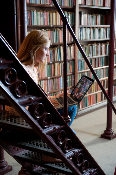 Young female student sitting on lattice staircase in an old library using a laptop computer --- Image by © Peter M. Fisher/Corbis